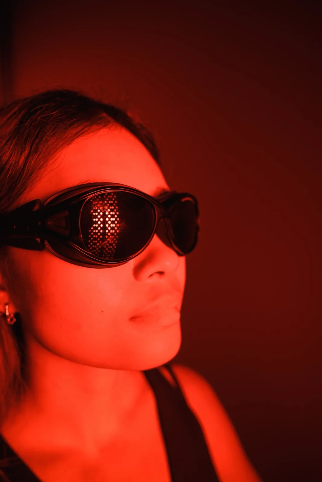 A guest wearing protective goggles beside red light panels