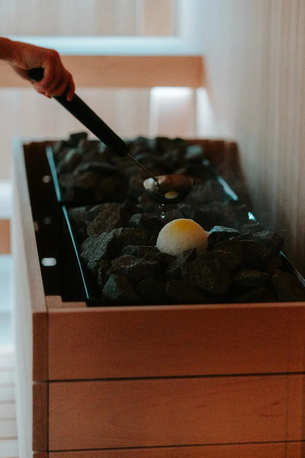 A sauna master ladling water over the glowing stove stones, steam rising in low firelight.